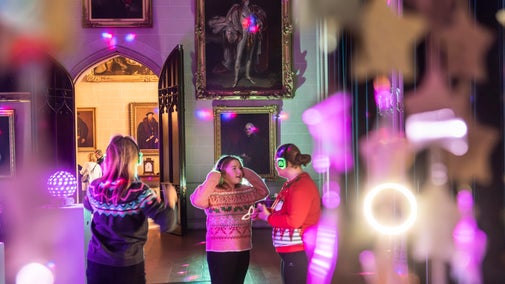 People with headphones dancing in a silent disco at Plas Newydd with disco lights reflecting on walls